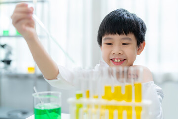 Young Asia kid doing experiment with foreigner teacher in the laboratory at school. Smart boy using dropper to transfer colorful solution into test tube. Chemical and learning elementary class