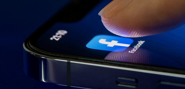 Finger touches the facebook application on mobile phone screen, Social media platform on smartphone on blue background.August 23, 2022, Bangkok, Thailand