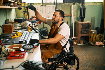 A bearded entrepreneur in a wheelchair works in his workshop. - 525361505
