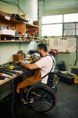 An entrepreneur in a wheelchair sits in a workshop and does manual work. - 525361566