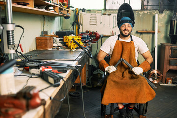 A portrait of a craftsman in a wheelchair wearing a welding helmet.