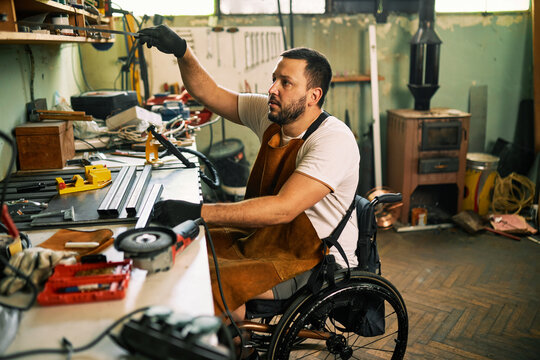 A bearded entrepreneur in a wheelchair works in his workshop.