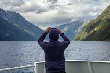 Norwegenreise -  Tourist steht am Heck einer Fähre und macht mit dem Handy Fotos der...