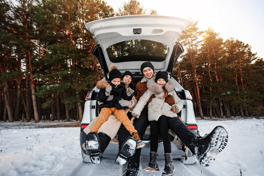 Family on winter walk. Happy young family having fun together. Parents sit with children in the trunk of car in winter forest. Warm winter boots close-up.