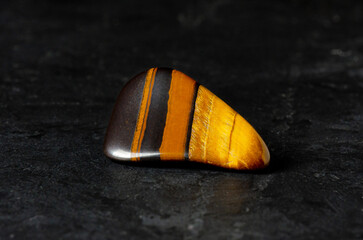 Tiger's eye mineral on a black concrete background. The concept of using minerals and crystals in astrology and alternative or complementary medicine.
