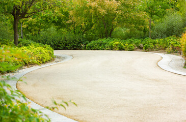 Empty winding asphalt road leaving over a horizon in urban city park, square. Lush green vegetation, deciduous trees in spring or summer day. Landscape design. A desert winding path without people.
