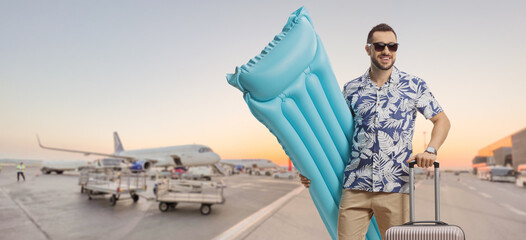 Young male tourist holding an inflatable mattress and posing on an airport
