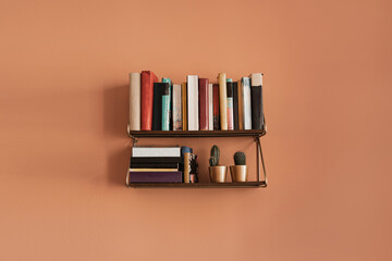 Books stack on hanging shelf. Coral peach wall background. Aesthetic minimal interior design....