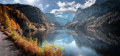 Wonderful autumn landscape. Popular alpine lake Grundlsee with colorful trees. Scenic image of forest landscape at sunny day. stunning nature background. Majestic Mountains on colorful scenery - 525365985
