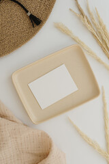 Paper sheet card with mockup copy space. Straw hat, muslin blanket, pampas grass stems, neutral beige plate