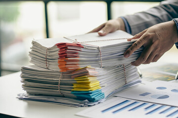 Businessman working in financial accounting with piles of documents on the desk at home work from home concept, business report, pile of unfinished paperwork
