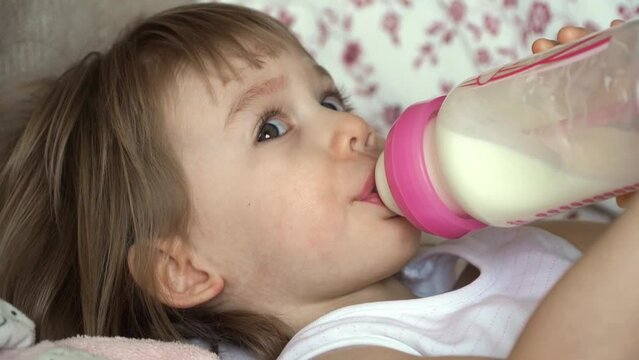 Close up little baby girl sucks bottle of milk. Child drinks infant formula. Baby food