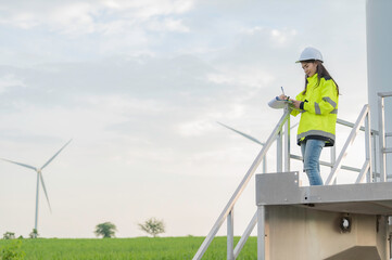 women engineer working and holding the report at wind turbine farm Power Generator Station on mountain,Thailand people