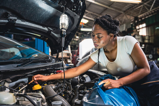 Female mechanic measuring the oil level of the car oil engine. - Powered by Adobe