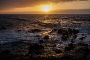 puesta de sol en la playa con un mar con olas rompiendo en las rocas de la costa