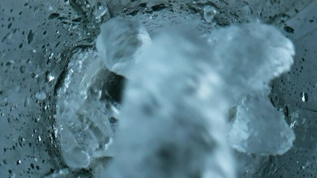 Ice cubes falling blender closeup. Grinding iced pieces in container top view.