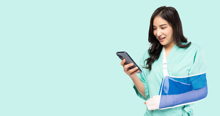 Young Asian woman put on soft splint due to a broken arm using phone isolated on green background...