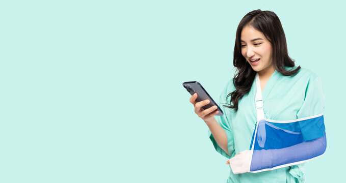 Young Asian woman put on soft splint due to a broken arm using phone isolated on green background Patient injured girl wearing patient outfits Insurance Health care and Personal accident concept