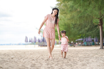 Asian young woman and her daughter walking and taking a view along the beach.