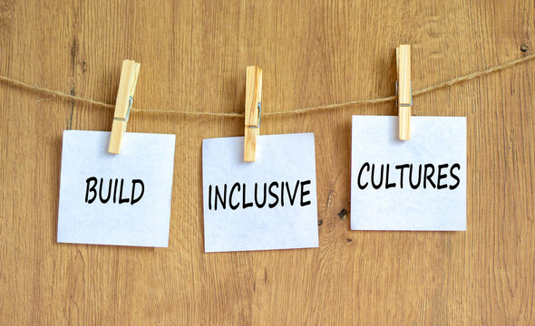 Build inclusive cultures and support symbol. Concept words Build inclusive cultures on white papers on clothespins. Beautiful wooden background. Business build inclusive cultures concept. Copy space.