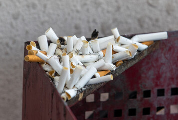 Many old cigarette stubs spilling over from ashtray of overflowing public trash bin stock photo