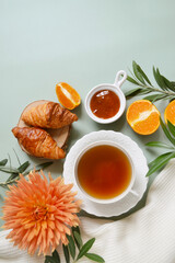 Cup of tea with jam and oranges on the pastel green background. Frame. Stay healthy in flu winter autumn days. Autumn fall tea composition with empty place for text. Calm cozy atmosphere. Village vibe