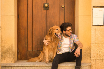 Young Hispanic man with beard and sunglasses sitting next to his dog on the front step of a house, very happy. Concept animals, dogs, love, pets, golden.