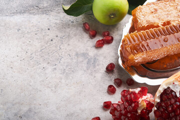 Rosh Hashanah. Honey jar, honeycomb, apple and pomegranate on gray old rustic concrete background table. Jewish New Year holiday greeting card. Rosh Hashanah holiday attributes. Space for text.