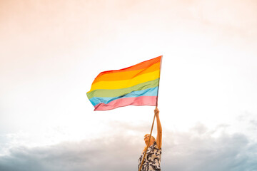 Senior woman waving rainbow flag outdoors at sunset