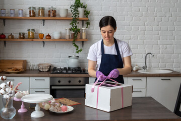 The pastry chef ties ribbon on the package with the cake for delivery. Selective focus. Photos about confectioners, food, hobbies.