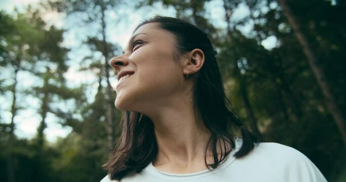Low angle young adult woman portrait shot in slow motion on summer vacation forest journey. Girl feeling free and happy on nature. Cheerful lady surrounded by trees enjoying of fresh air