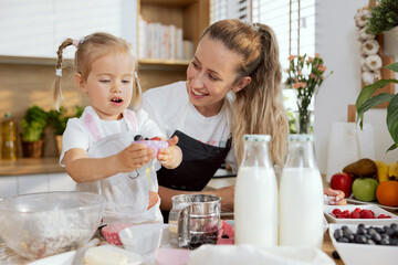 Curious little kid with two pigtails with pretty mom showing homemade muffin talking. Baking cooking preparing surprise for family breakfast