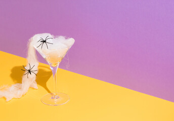 Halloween spooky concept with martini glass, spider web and spiders on purple and ocher background....