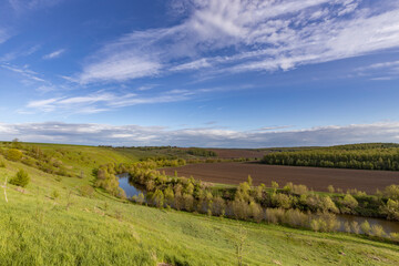 Fototapeta premium View of the countryside. bright greenery in the ravine. Saturated green grass against the blue sky. Plowed field on the horizon.