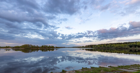 Evening landscape, sunset on the river. Wide river, horizon, clouds are reflected in the water.