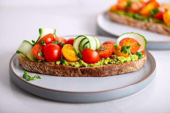 Tasty Open Sandwich From Toasted Sourdough Bread With Mashed Avocado, Slices Of Fresh Cucumber And Cherry Tomatoes