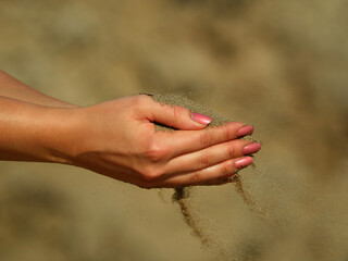 female hand filled with sand and wind blows sand away