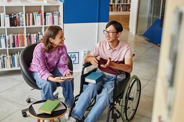 High angle portrait of Asian young man in wheelchair talking to friend while studying together in...