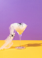 Spooky idea with martini glass, spider's web and spiders on purple and ocher background. Creative...