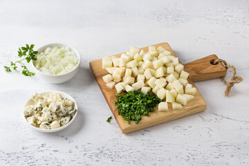 Preparation of pear and blue cheese risotto: board with chopped pear and parsley, chopped onion and blue cheese on a light gray background