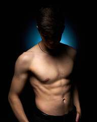 a healthy athletic teenager shows off his body against a dark background, the concept of proper...