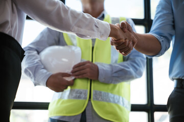 Close up of handshaking of engineer and architect after on paperworks and floor plan drawings about design and building houses.