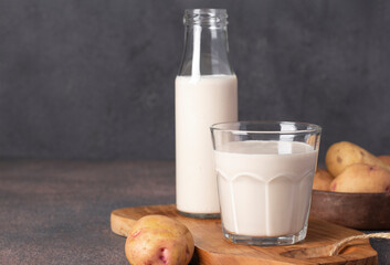 Vegan potato milk in a bottle and glass, as well as potatoes in a plate on dark gray background. Plant-based, lactose-free milk replacer