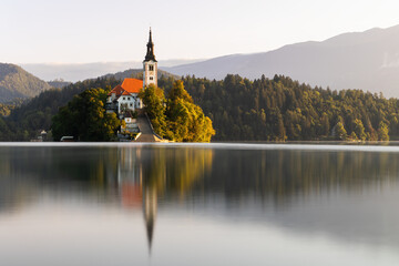 A church in the middle of an Bled lake in Slovenia at sunrise. Tourist destination with historic building set into lovely nature surrounding with reflection on water surface.