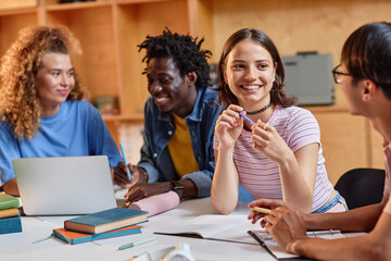 Diverse group of students working at table in library together, focus on smiling young woman...