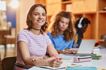 Diverse group of students in row studying in college library, focus on smiling young woman looking at camera in foreground, copy space