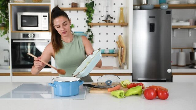 Young sporty woman cutting and cooking fresh natural vegetables at kitchen and cooking for healthy lunch. Self care yoga nutritionist girl having healthy meal after workout.