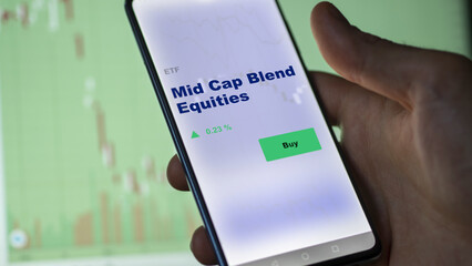 An investor's analyzing the mid cap blend equities etf fund on screen. A phone shows the ETF's prices midCap equity to invest