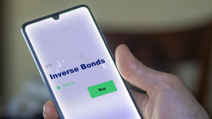 An investor's analyzing the inverse bonds etf fund on screen. A phone shows the inv bond ETF's prices stocks to invest