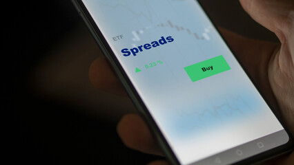 An investor's analyzing the spreads etf fund on screen. A phone shows the ETF's prices to invest